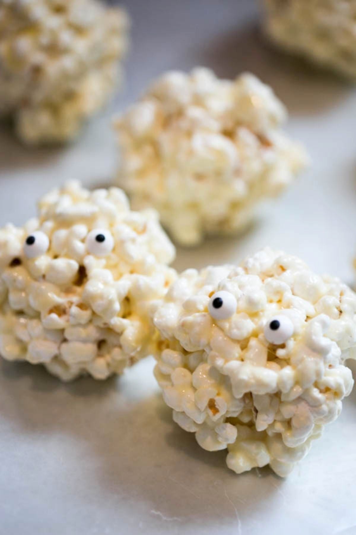 Two popcorn balls with googley eyes on them for a Halloween treat sitting on a counter.