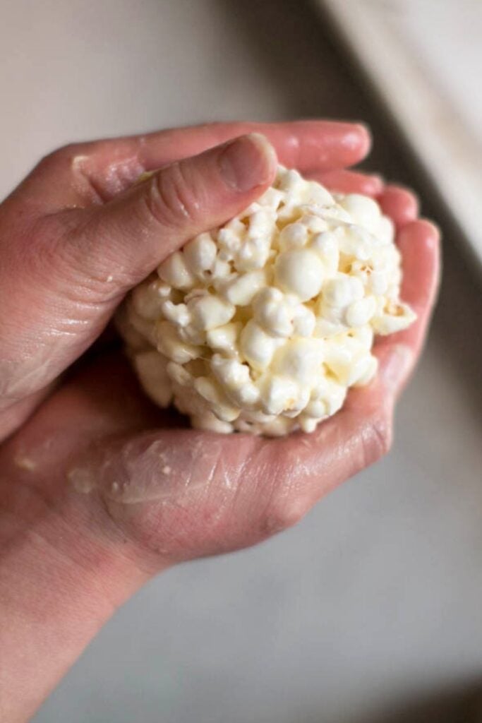 Two hands holding a sticky popcorn ball over a tray.