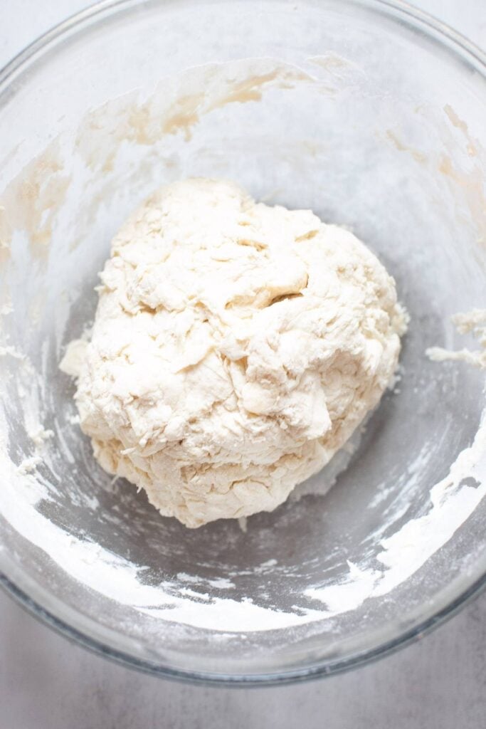 A shaggy ball of sourdough bagel dough in a glass bowl.