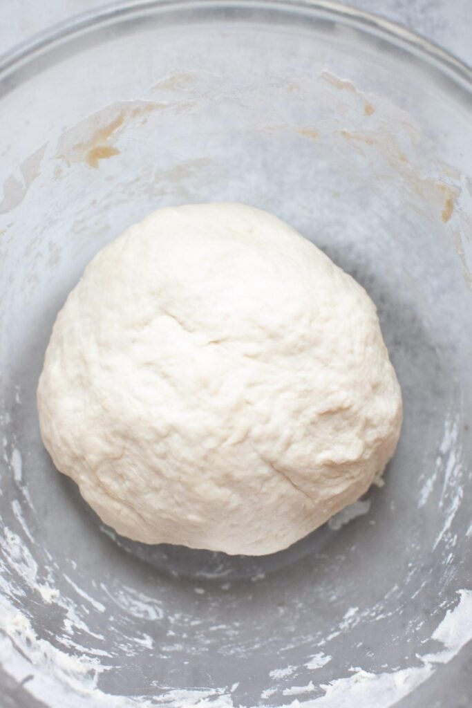 A smooth ball of bagel dough in a bowl sitting on a counter.