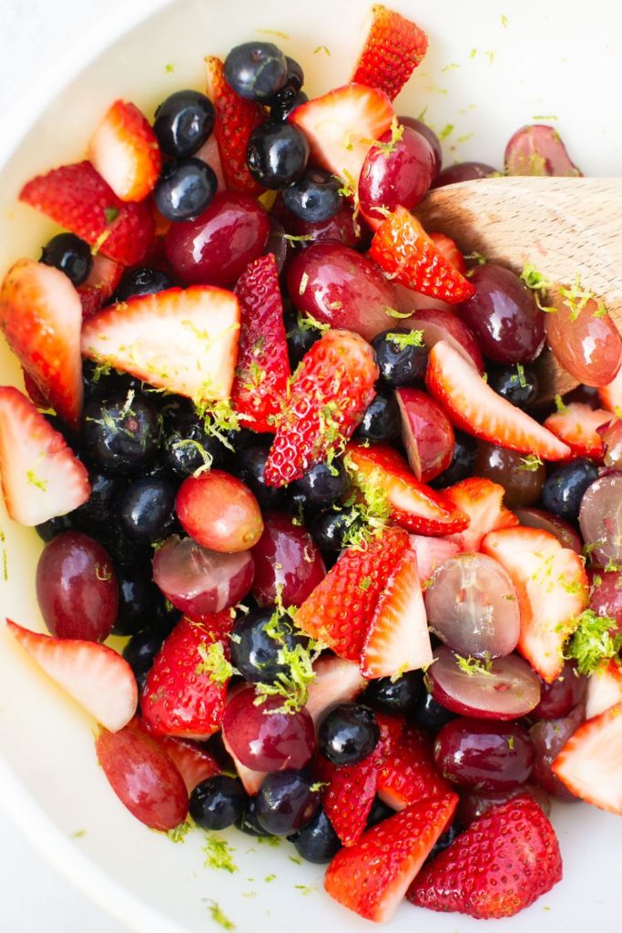 honey lime fruit salad featuring strawberries, blueberries and grapes in a bowl.