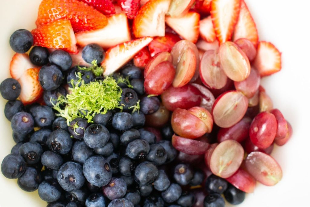 blueberries, grapes and strawberries in a bowl being mixed together for a fruit salad.