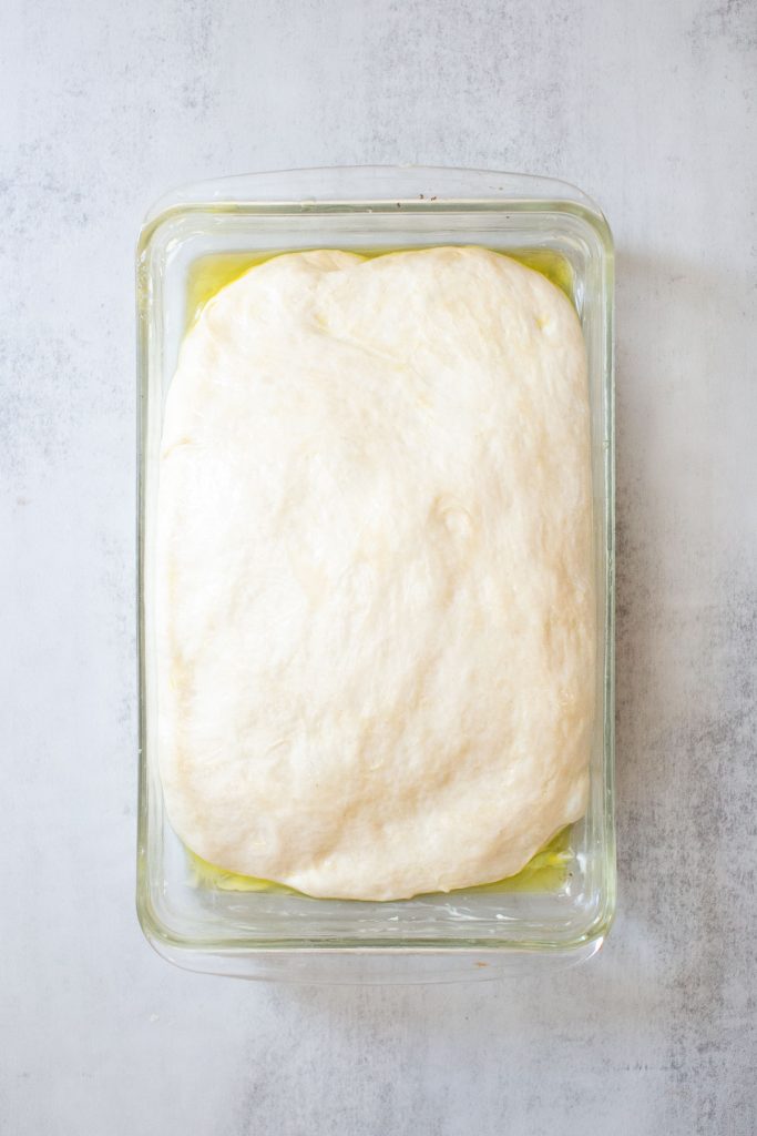 sourdough focaccia bread rising in a baking dish