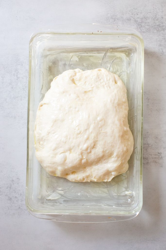 sourdough focaccia bread rising in a baking dish