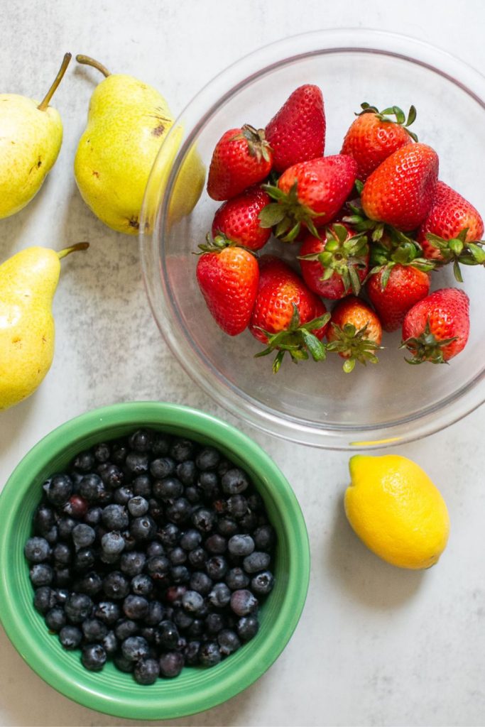 ingredients for red white and blue fruit salad: strawberries, blueberries pears and a lemon.