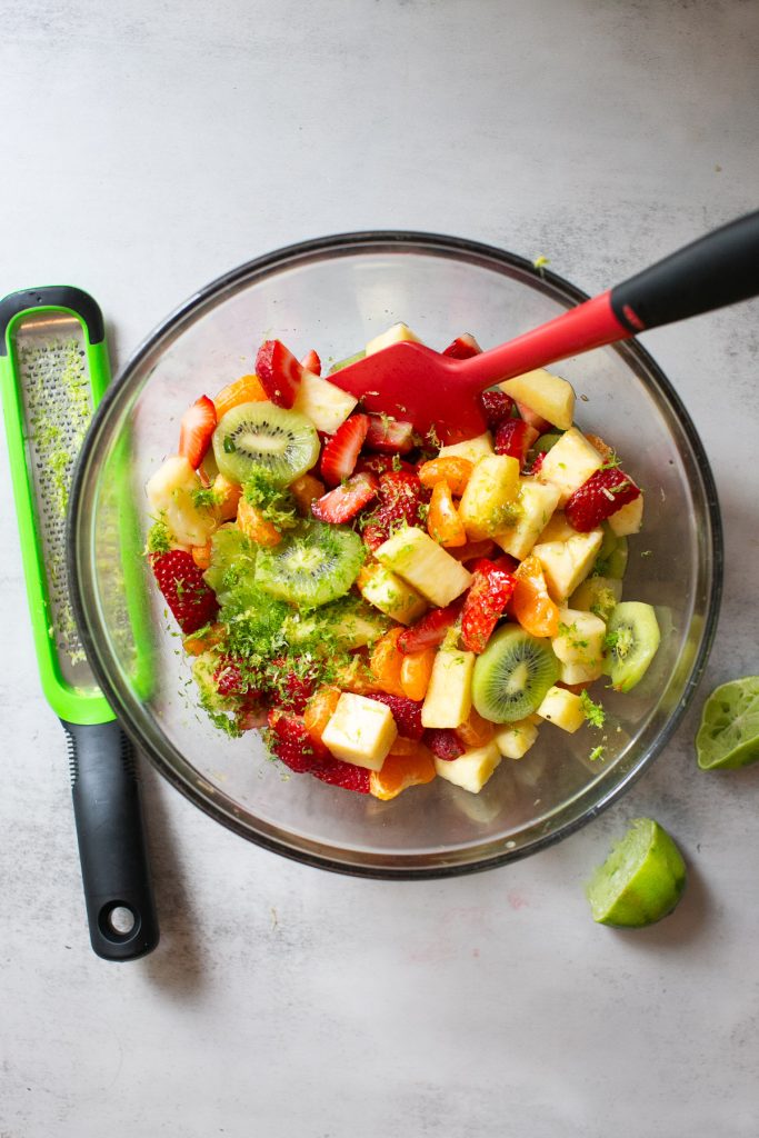 lime zest being added to a tropical fruit salad