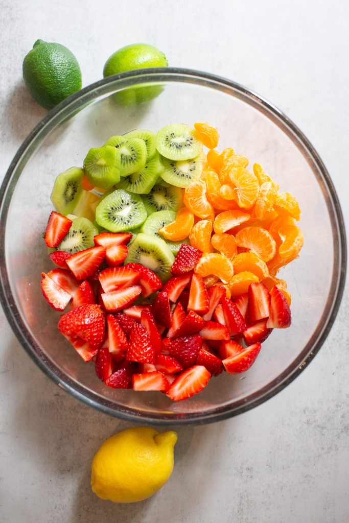 strawberries, kiwi, and oranges being mixed into a bowl
