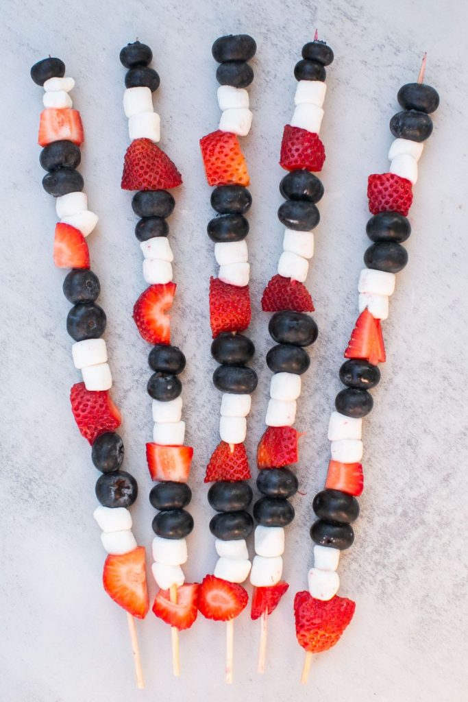 red, white and blue fruit skewers made out of marshmallows, strawberries and blueberries on a tray