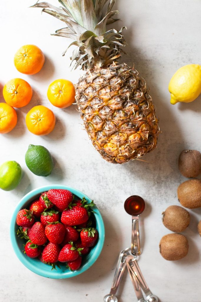 ingredients for tropical fruit salad on a plate: oranges, limes, honey, lemon s, pineapple and kiwi