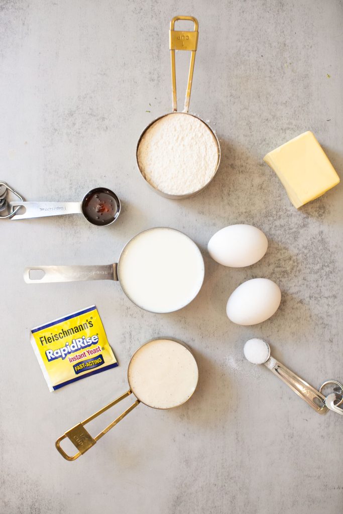 ingredients for sourdough discard hamburger buns: flour, warm milk, eggs, butter, sourdough discard, salt, and honey and rapid rise yeast