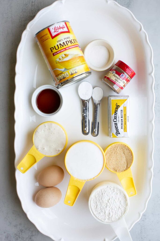 ingredients for pumpkin streusel muffins: pumpkin pie puree, pumpkin spice, sourdough discard, vanilla extract, eggs, butter, sugar, baking powder and milk on a table