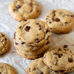 A piece of parchment paper with a stack of brown butter sourdough discard chocolate chip cookies on it.