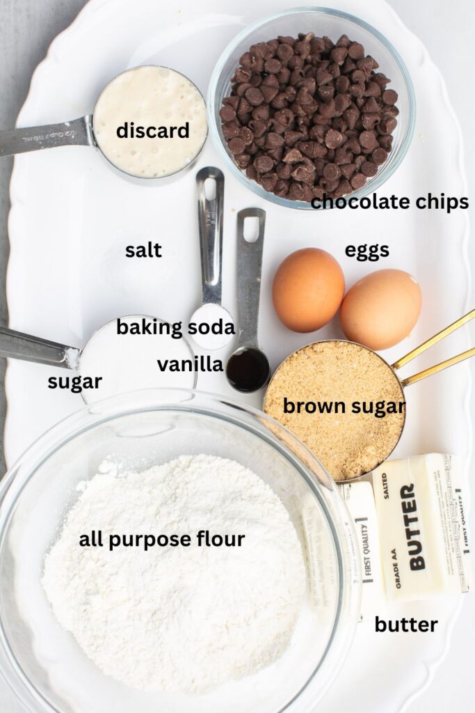 ingredients for browned butter sourdough chocolate chip cookies on a tray: sourdough discard, chocolate chips, eggs, salt, baking soda, sugar, vanilla, brown sugar, butter and flour