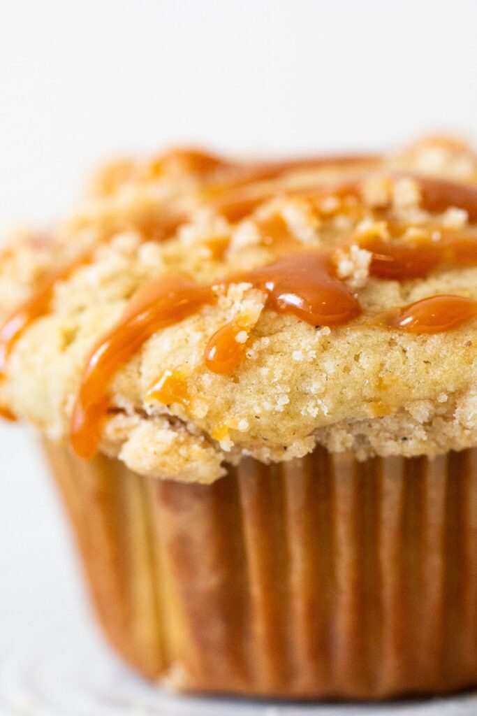 up close photo of an apple muffin dripping with caramel sauce and crumb topping