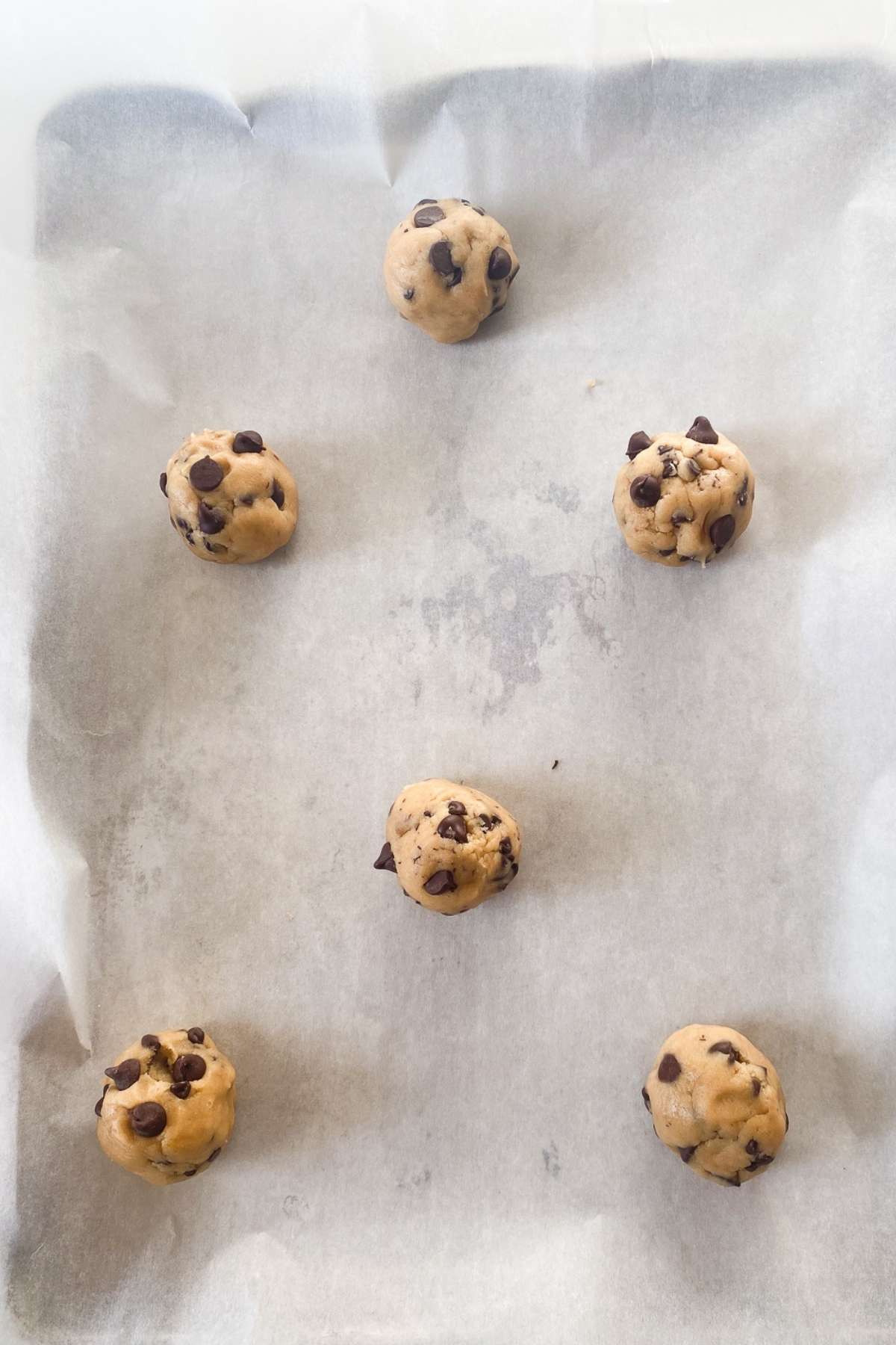 Balls of sourdough discard chocolate chip cookies made with brown butter on a baking tray lined with parchment paper.