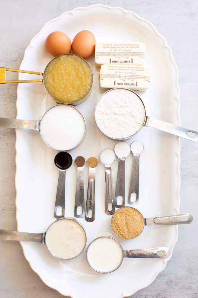 ingredients for sourdough discard caramel apple muffins on a tray: eggs, butter, apple sauce, all purpose flour, sourdough discard, sugar, vanilla, nutmeg, brown sugar, discard, and cream