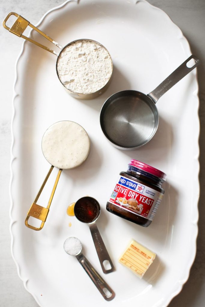 ingredients for sourdough discard sandwich bread on a platter: flour, water, sourdough starter, active dry yeast, butter, honey and salt