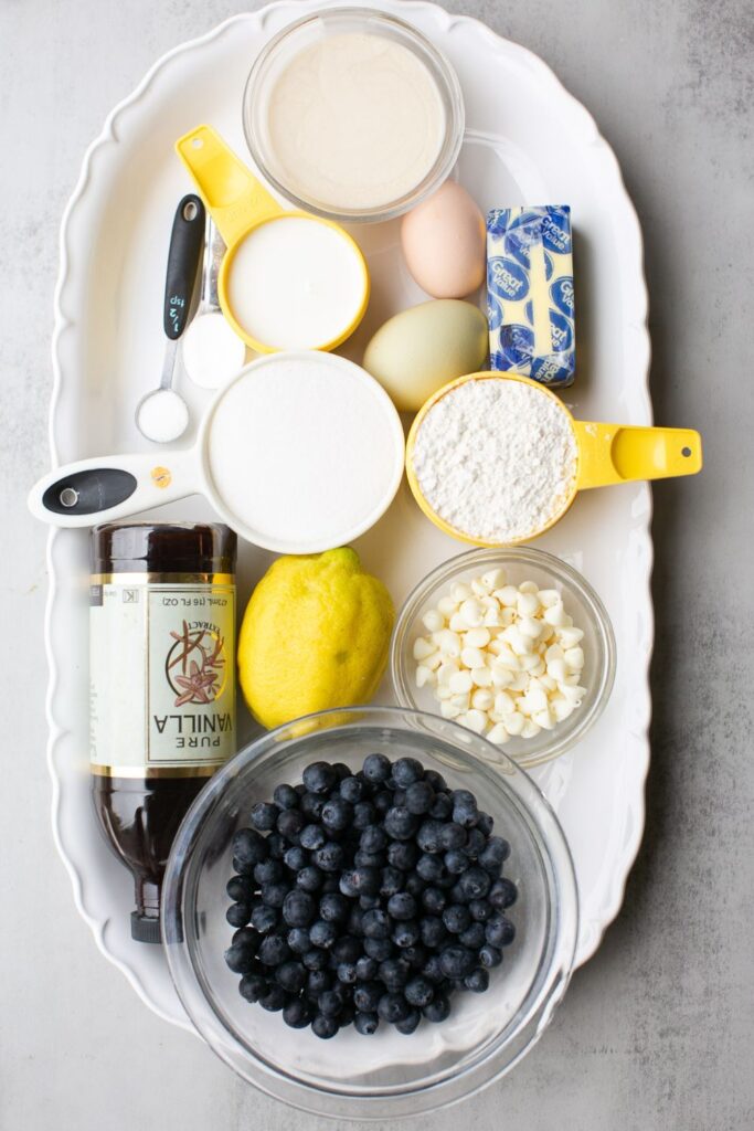 ingredients for white chocolate blueberry muffins on a tray: sourdough discard, lemon, eggs, butter, salt, baking soda, blueberries, white chocolate, and vanilla extract