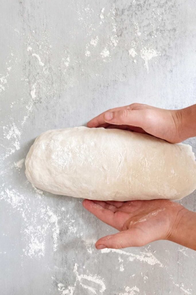 Sourdough sandwich bread dough rolled into a log on a table.