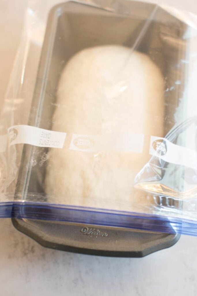 Sourdough sandwich bread dough in a 9x5 inch loaf pan covered with plastic wrap.