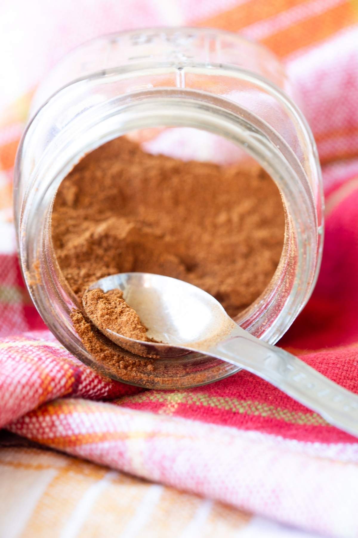 Homemade pumpkin pie spice blend in a jar on a red and orange table cloth.