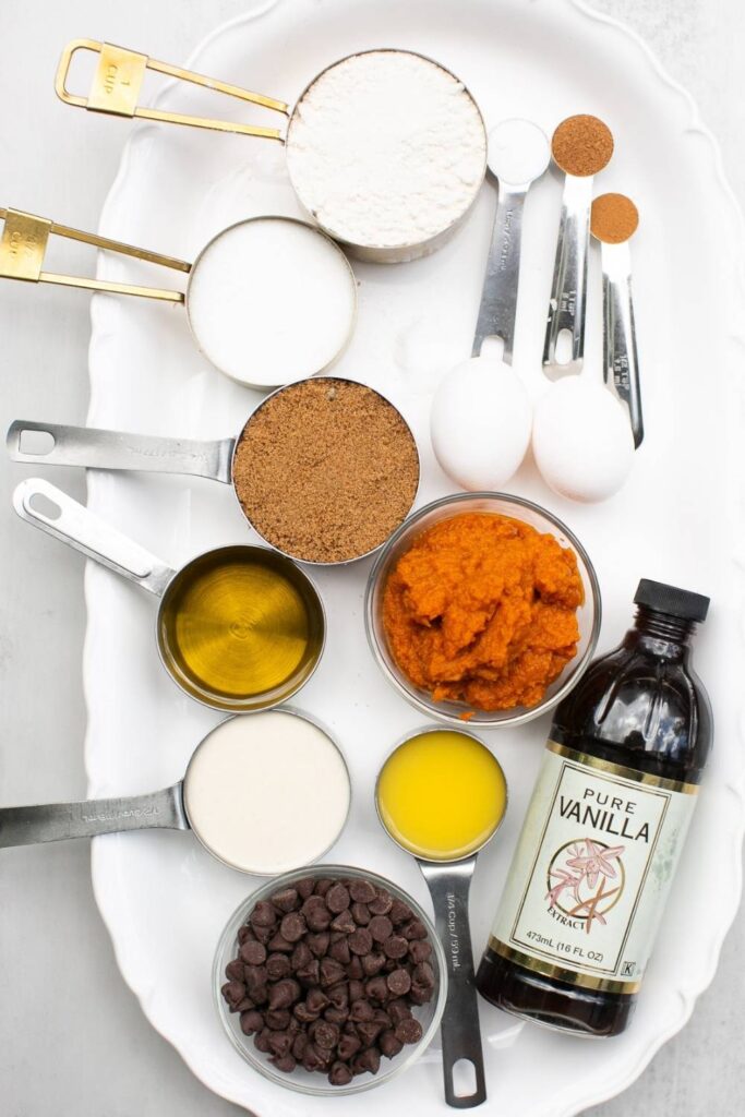 ingredients for sourdough discard pumpkin bread on a plate:  brown sugar, white sugar, vanilla extract, orange juice, sourdough discard, pumpkin puree, eggs, pumpkin pie spice and flour