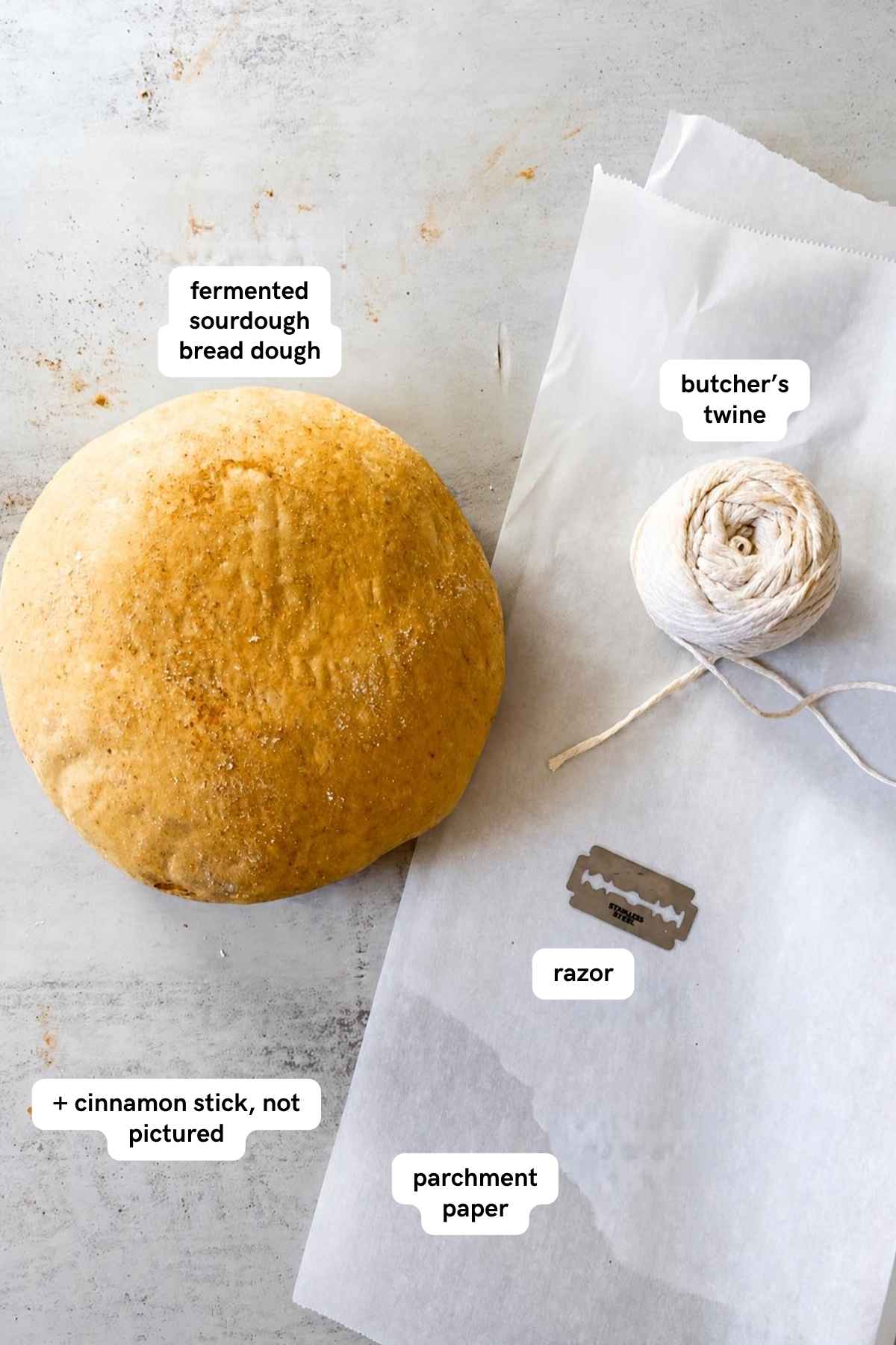 Ingredients for pumpkin shaped sourdough bread loaf on a tray: sourdough bread boule, butcher's twine, parchment paper and cinnamon stick.