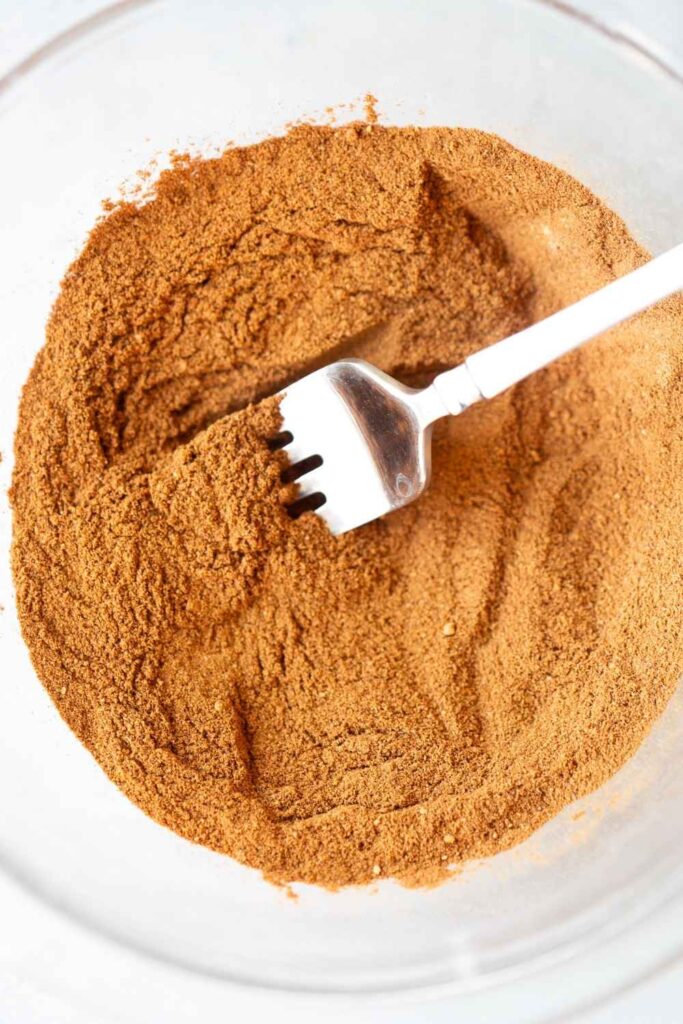 spices for pumpkin pie spice being mixed in a small bowl with a fork. 
