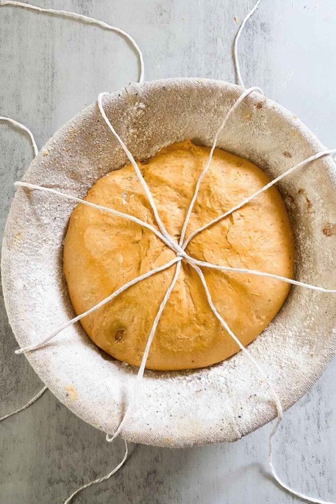 Sourdough bread dough in a banneton with butcher's twine draped over it in sections of 8.