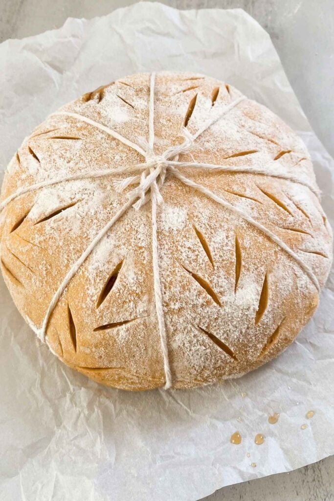 A loaf of sourdough bread with twine wrapped around it for a pumpkin shaped loaf, with sourdough scores down the side.