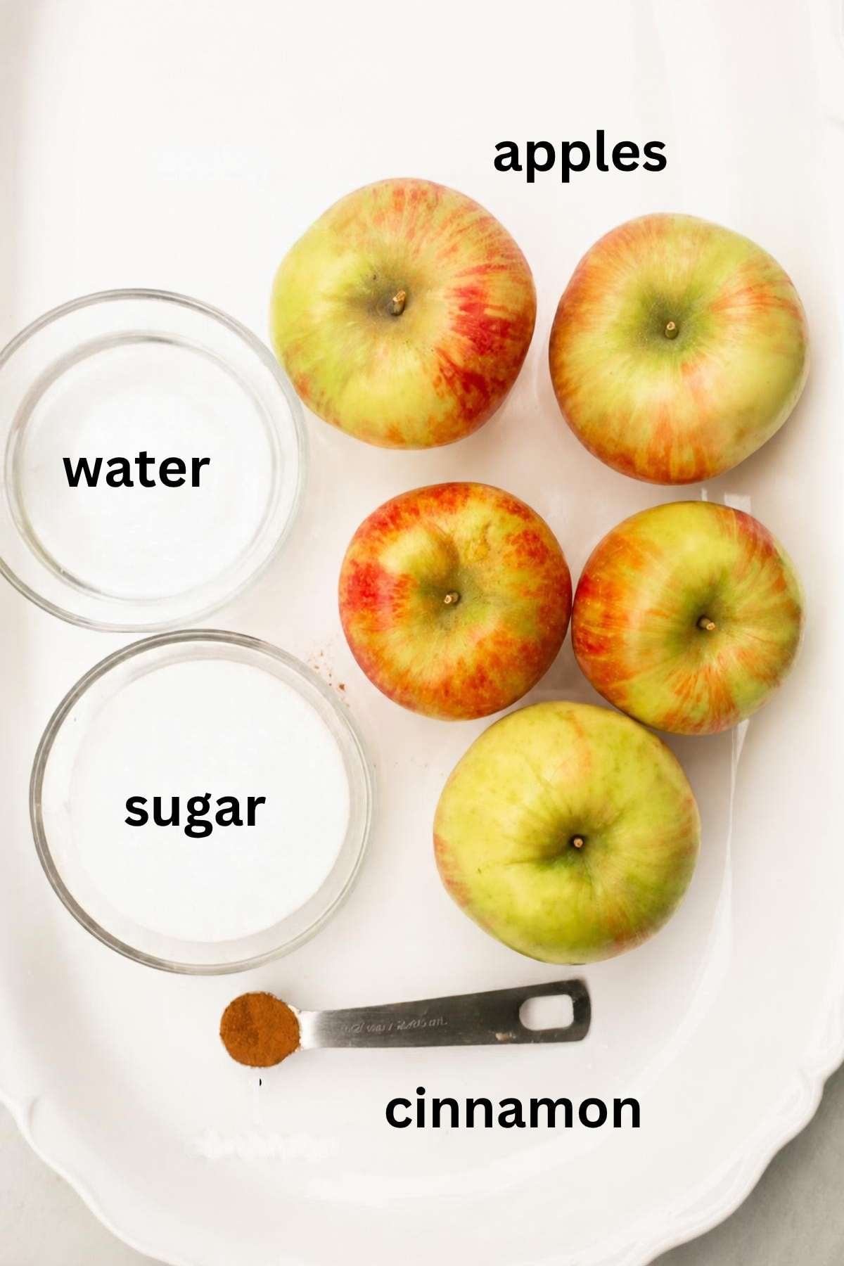 ingredients for homemade applesauce on a tray: sugar, apples, water, and cinnamon.