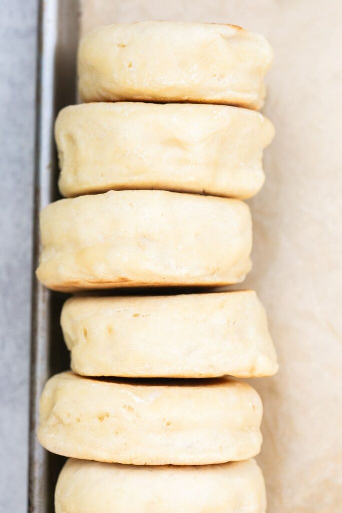 a stack of sourdough English muffins on a baking pan