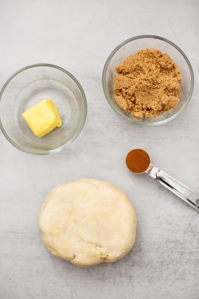 ingredients for pie crust cookies on a tray: butter, cinnamon, brown sugar, and flaky pie crust
