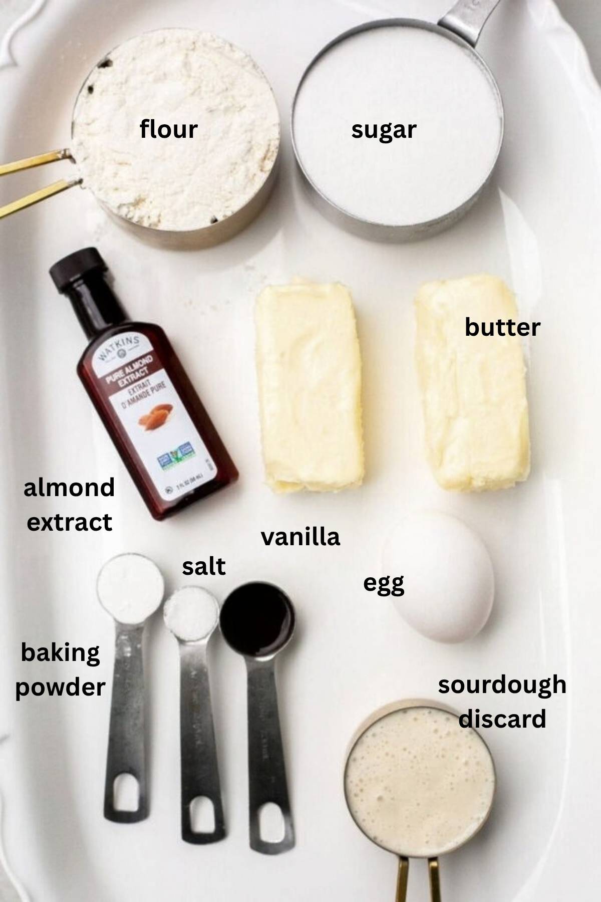 Ingredients for sourdough discard cut out sugar cookies on a tray: almond extract, butter, sourdough discard, egg, vanilla, salt, baking powder, and flour.