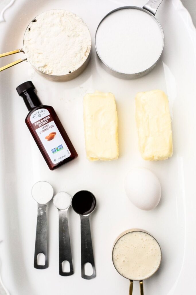 ingredients for sourdough discard sugar cookies on a plate: vanilla, flour, butter, eggs, sourdough discard and baking powder on a tray