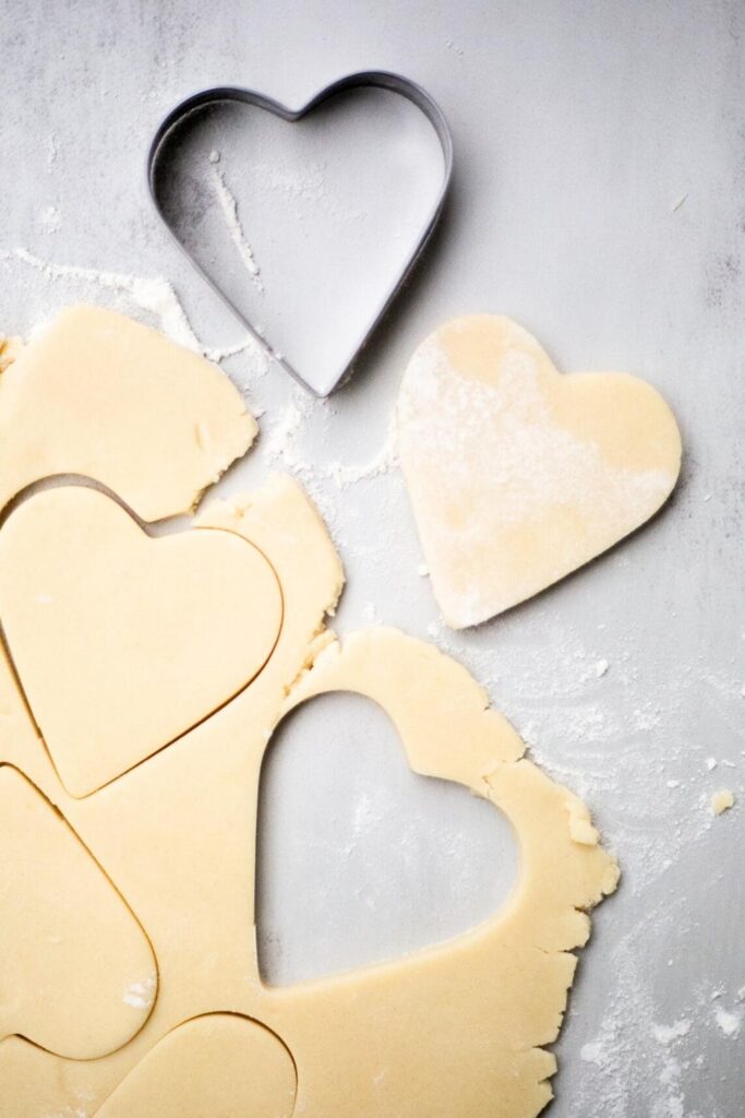 heart shaped sugar cookie dough being cut out with a cookie cutter