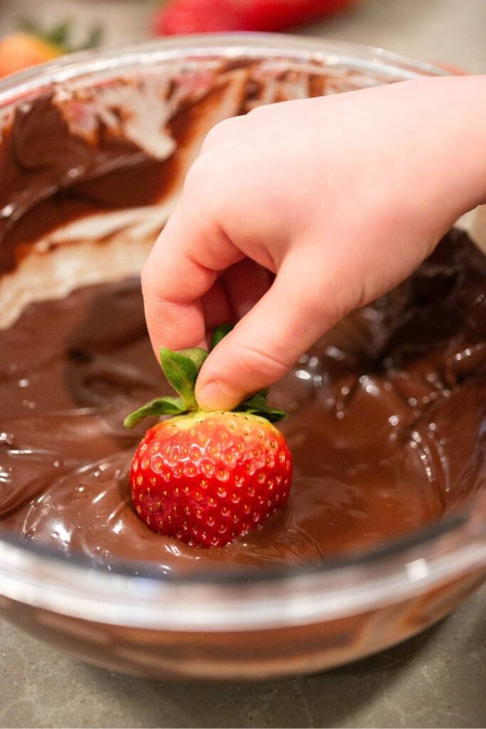 a strawberry being dipped into melted chocolate by the stem
