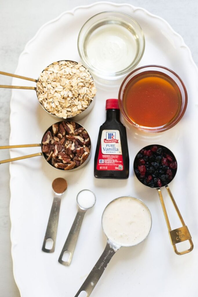ingredients for sourdough discard granola on a tray: oats, sourdough discard, honey, dried fruit, pecans, vanilla, cinnamon, and salt
