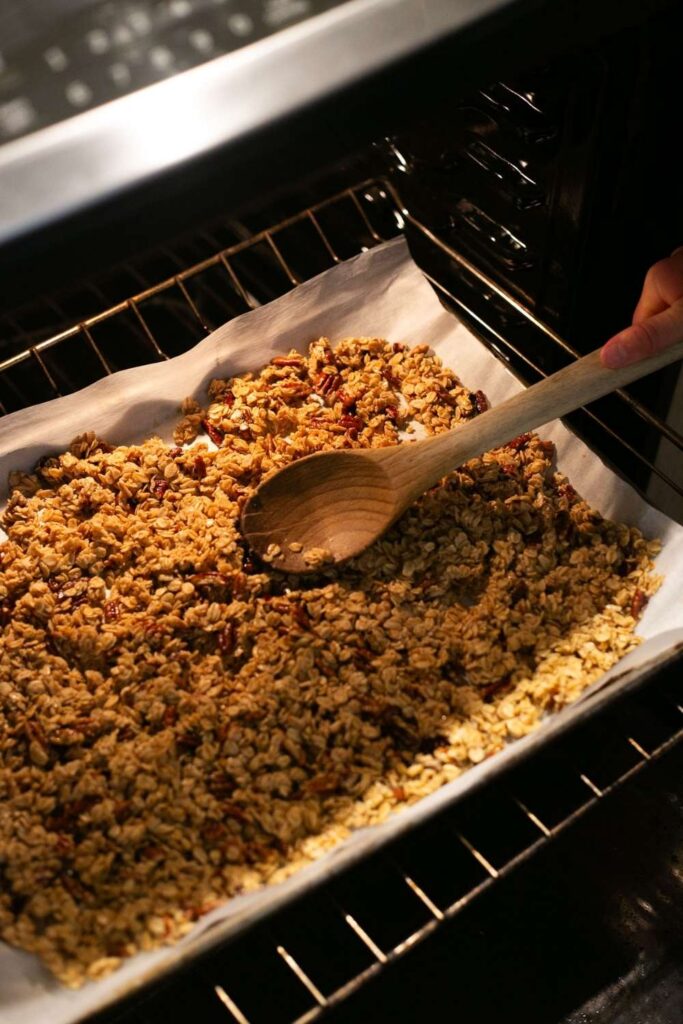 sourdough discard granola being patted down in oven to promote clumping