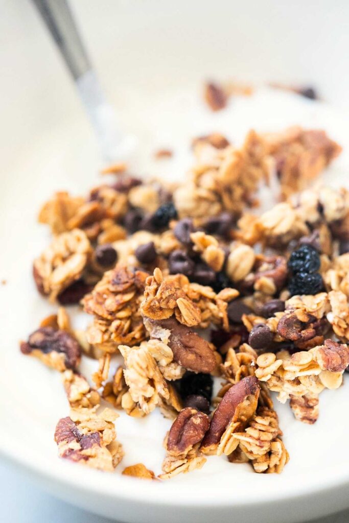 Sourdough discard granola served over a bowl of yogurt with a metal spoon.