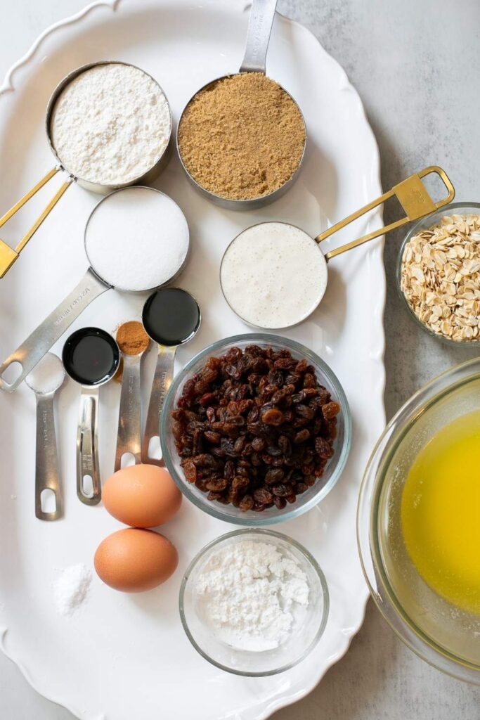 ingredients for sourdough discard oatmeal cookies on a tray: brown sugar, white sugar, raisins, oatmeal, molasses, sourdough discard, flour, salt, melted butter , eggs and oats