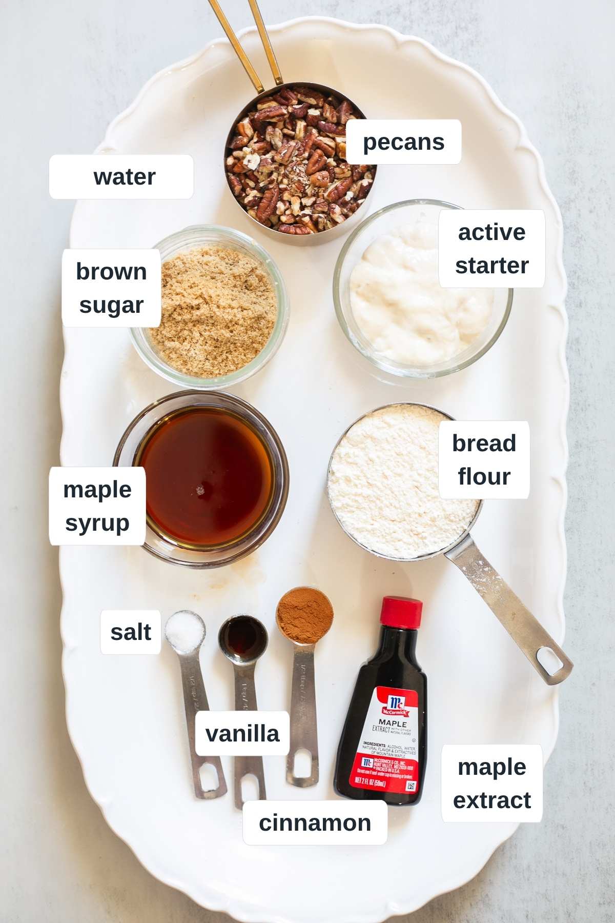 Ingredients for sourdough maple pecan bread loaf on a tray: pecans, brown sugar, active starter, maple syrup, vanilla, maple extract, salt, and flour.
