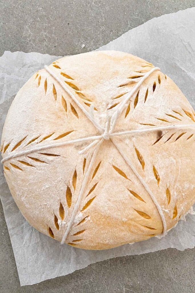 A loaf of sourdough artisan bread that has been scored on a counter.